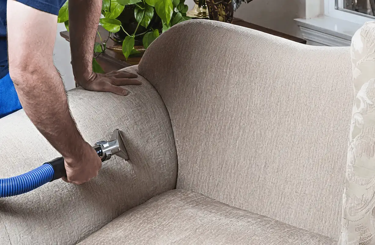 Professional upholstery cleaner deep-cleaning a fabric sofa with a handheld extraction tool and hose, Naperville, IL.